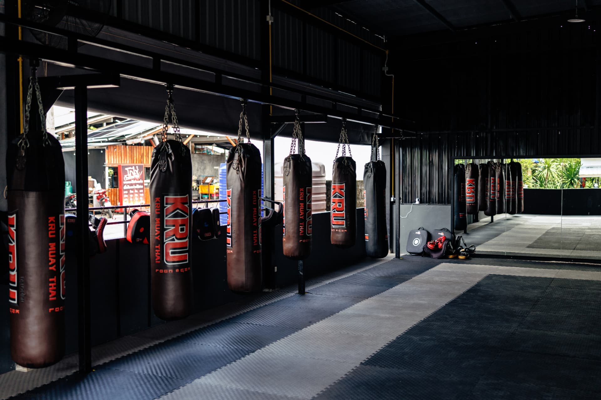 KRU branded heavy bags hanging in a row along the open-air training floor at Kru Muay Thai Gym